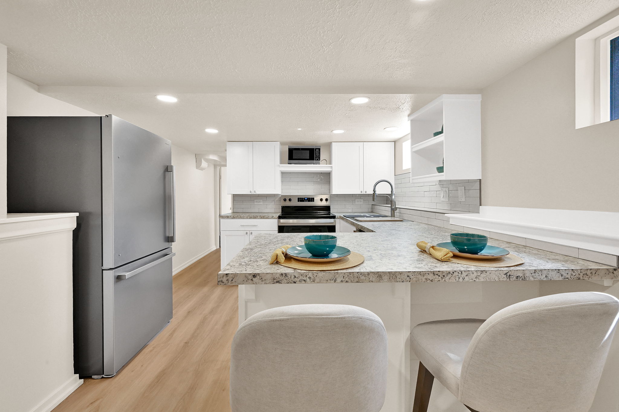 Modern kitchen featuring white cabinetry, granite countertops, subway tile backsplash, and wood-finish flooring