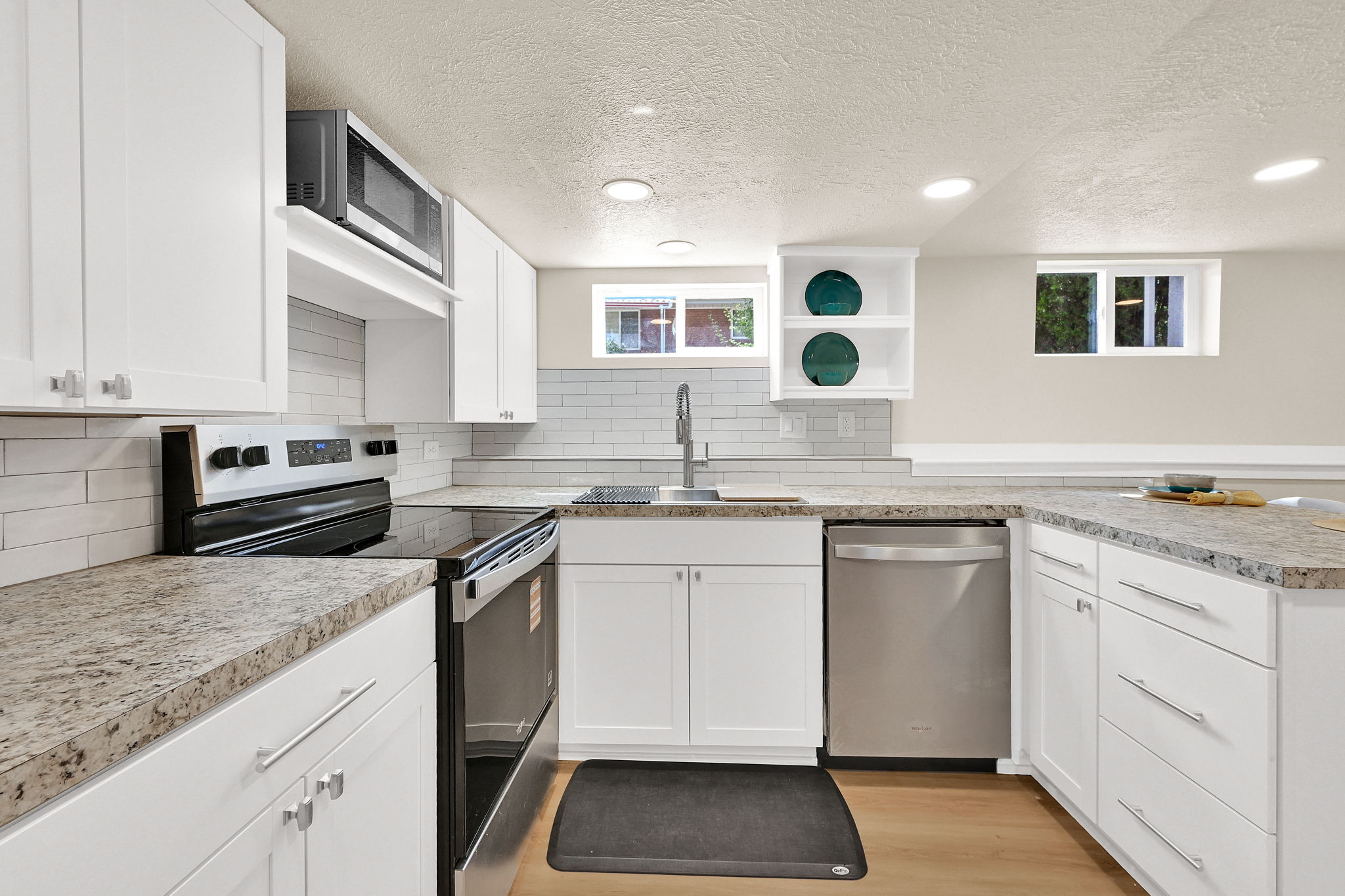 Bright kitchen featuring abundant white cabinetry, light wood-finish flooring, recessed lighting, and stainless steel appliances including a built-in microwave, range, and dishwasher