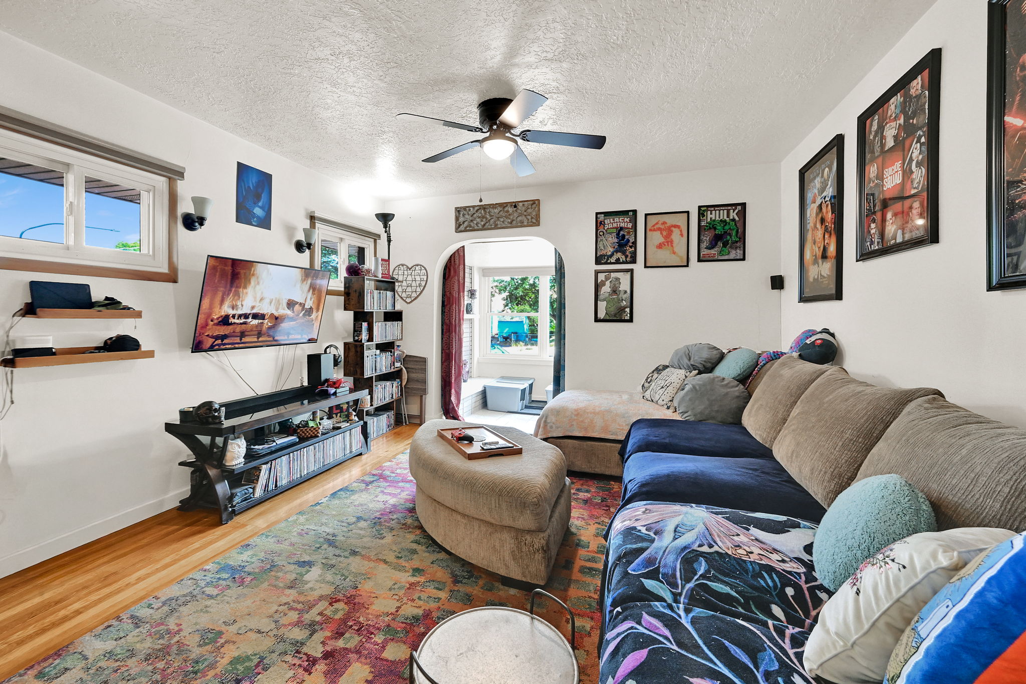 Spacious living area featuring wood-finish flooring, a ceiling fan, and multiple windows for natural illumination