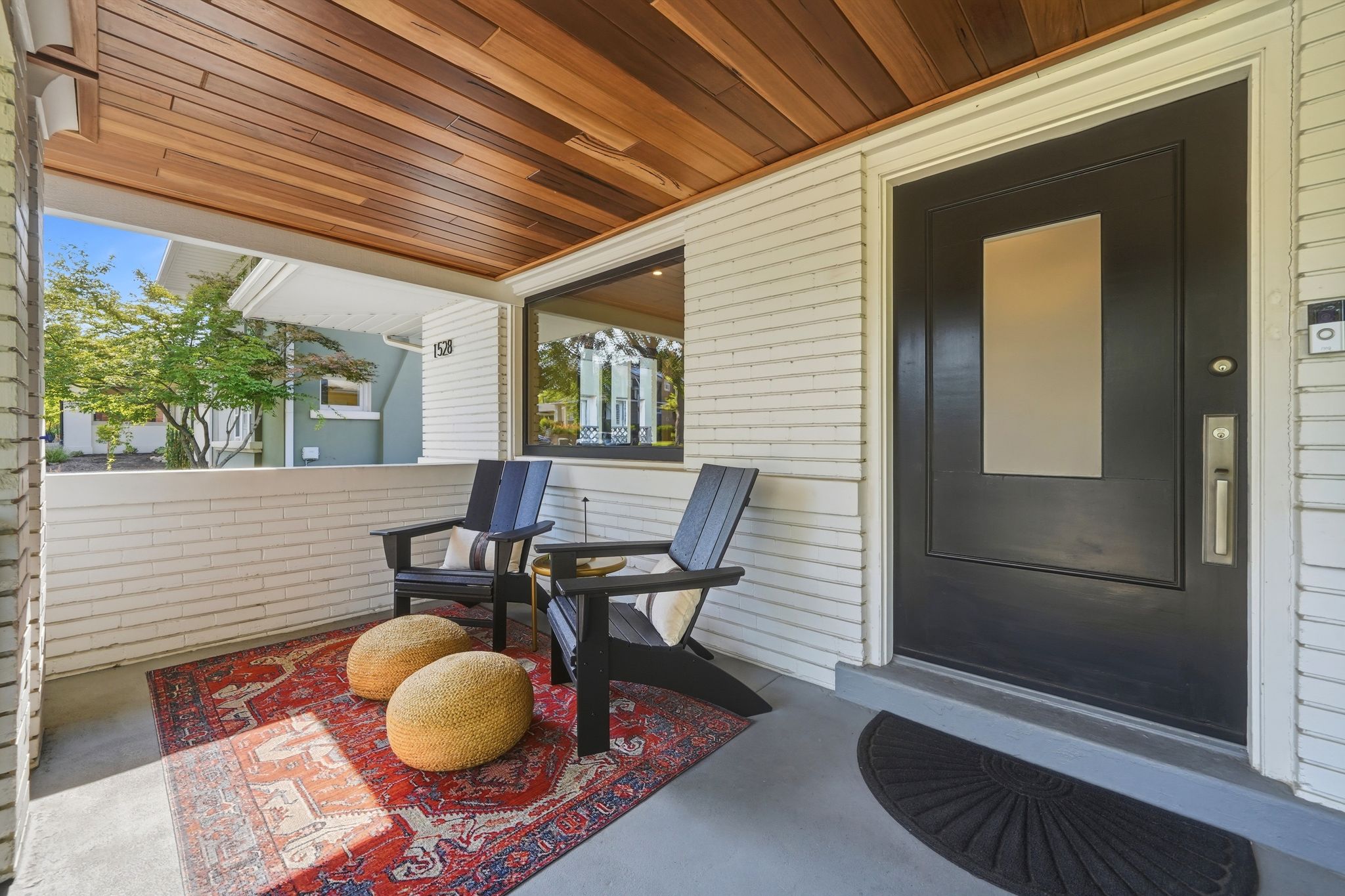 Inviting covered porch with a wood-finish ceiling, white horizontal siding, and a dark entry door with frosted glass