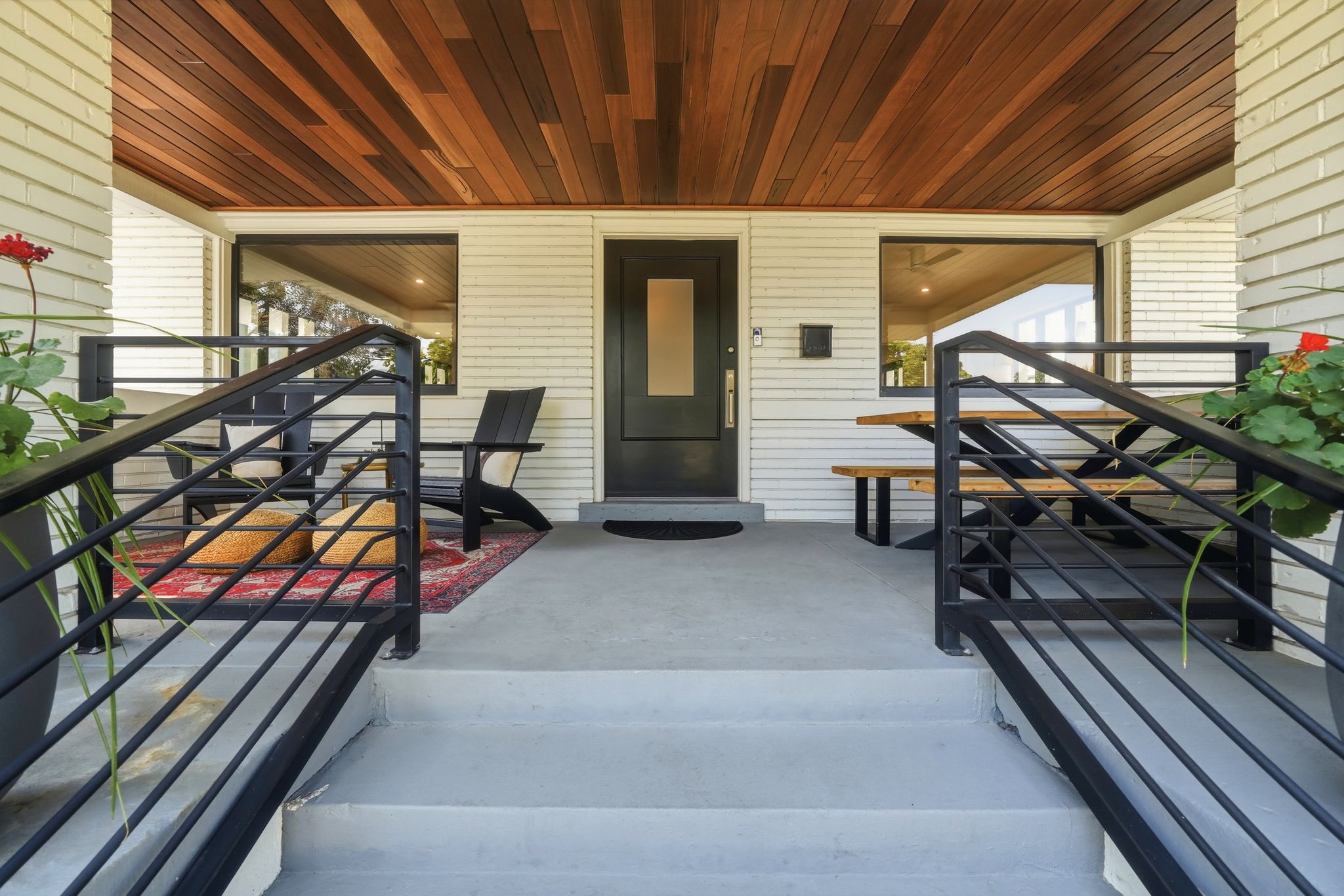 Covered front porch featuring a wood-finish ceiling, black framed windows, and modern metal railings