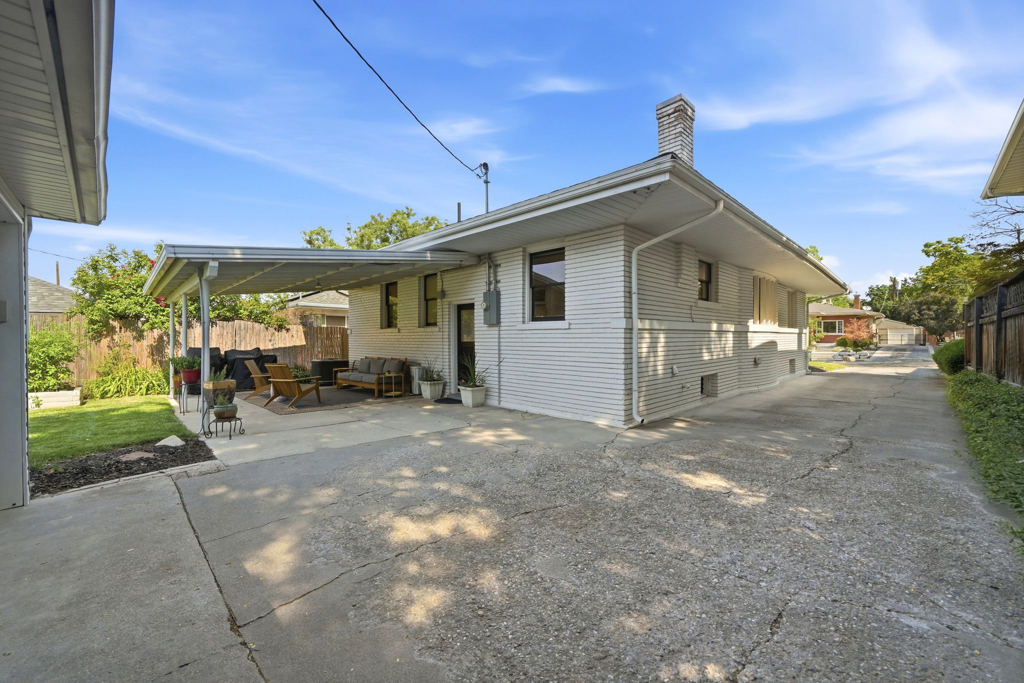 Expansive concrete driveway alongside a structure featuring white siding and a covered patio area