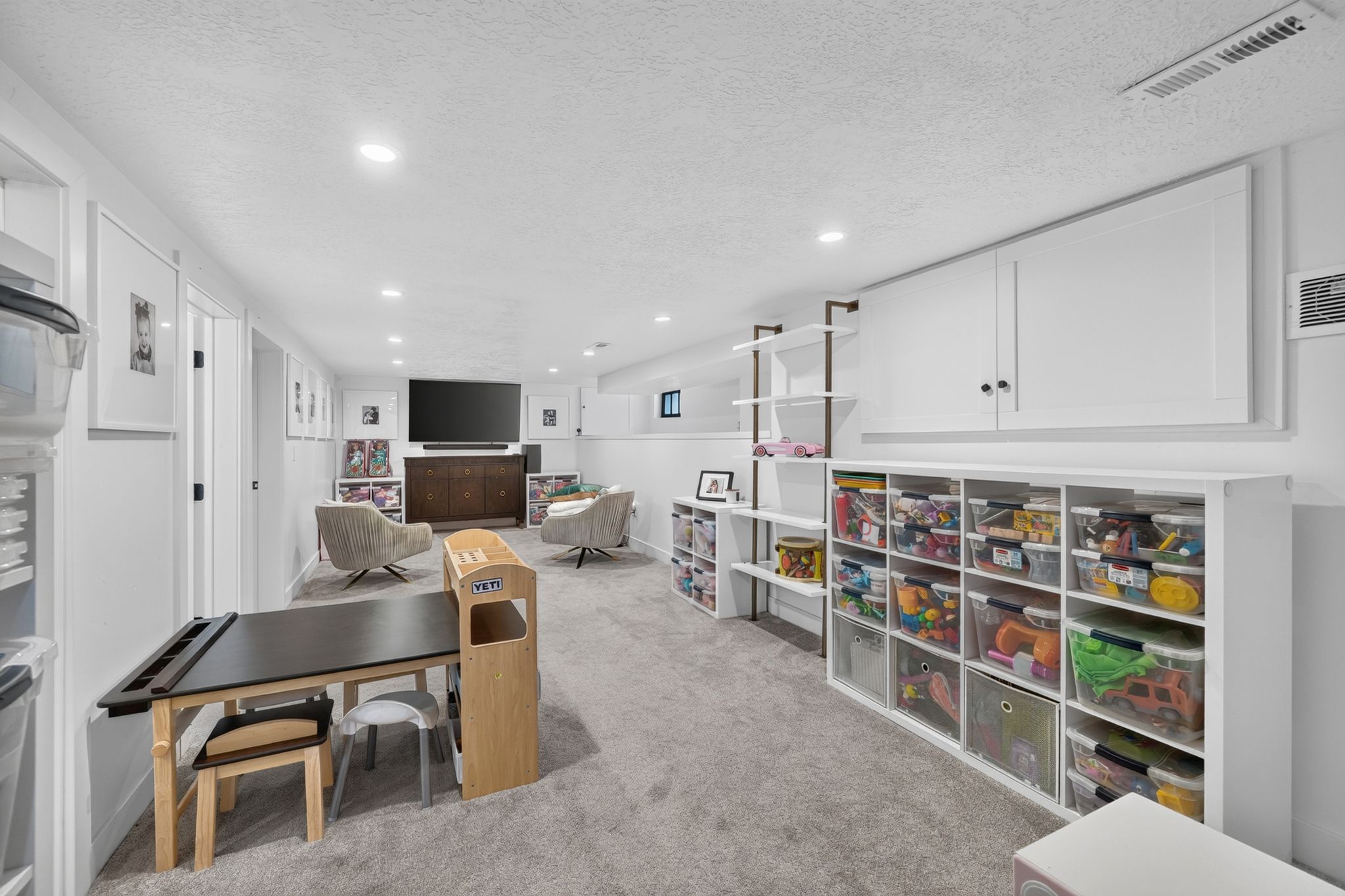 Versatile lower-level space featuring recessed lighting, plush carpet flooring, white painted walls, and extensive built-in cabinetry with black hardware