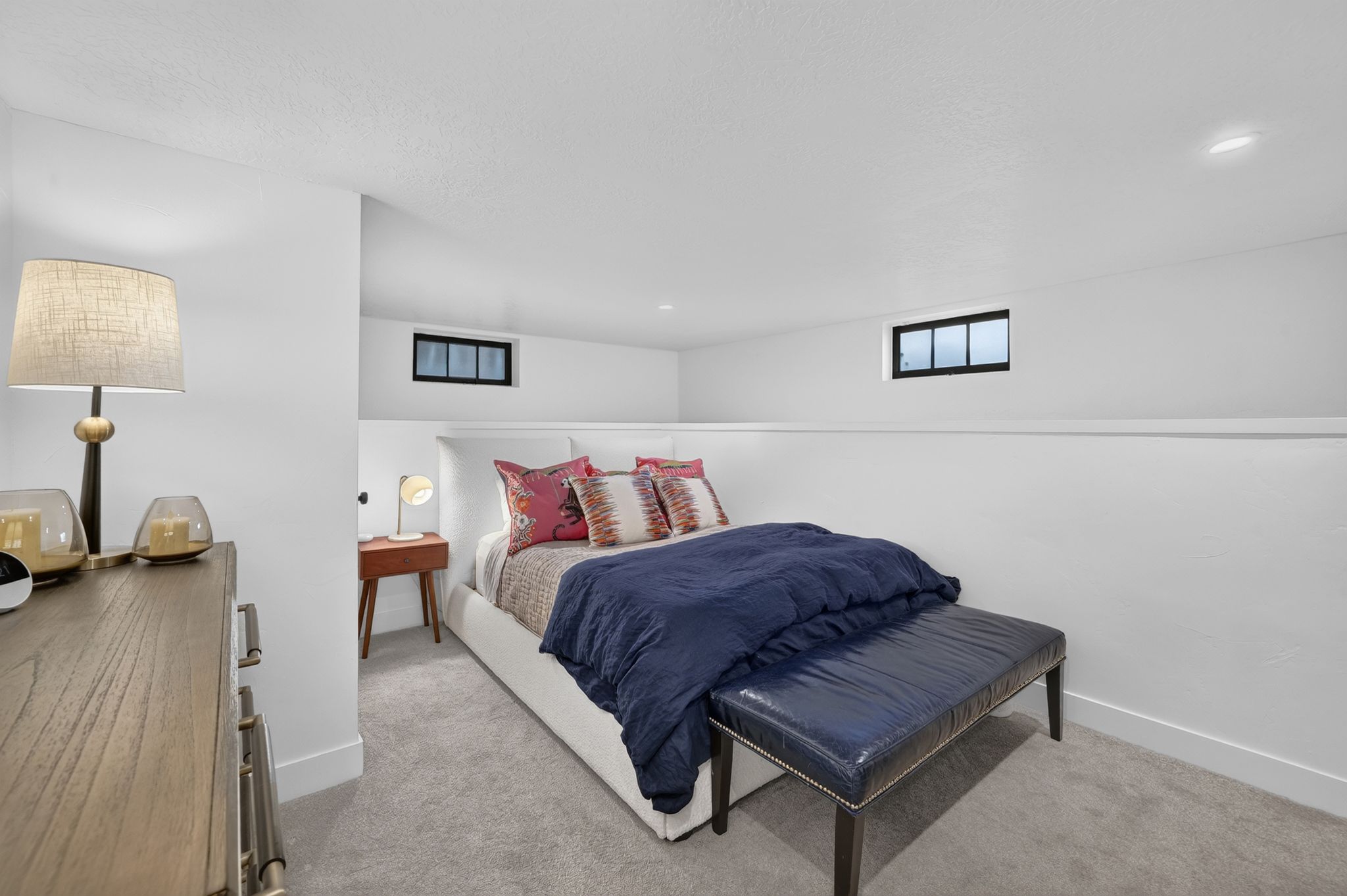 Carpeted sleeping area with recessed lighting, white walls, and two high-set windows featuring black trim
