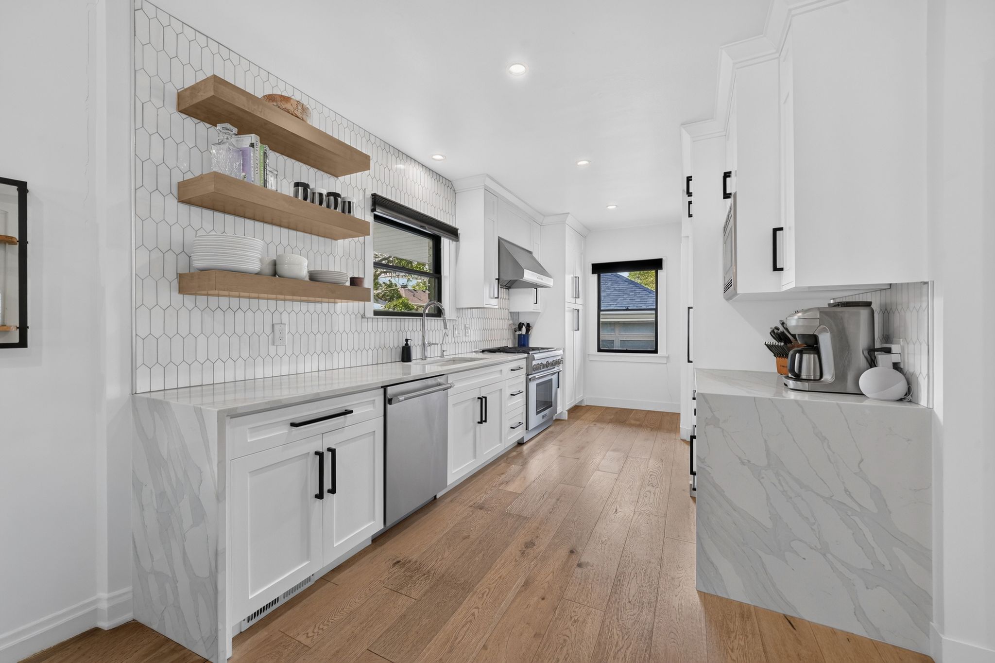 Modern kitchen featuring white cabinetry, wood-finish flooring, stainless steel appliances, and a pickett tile backsplash