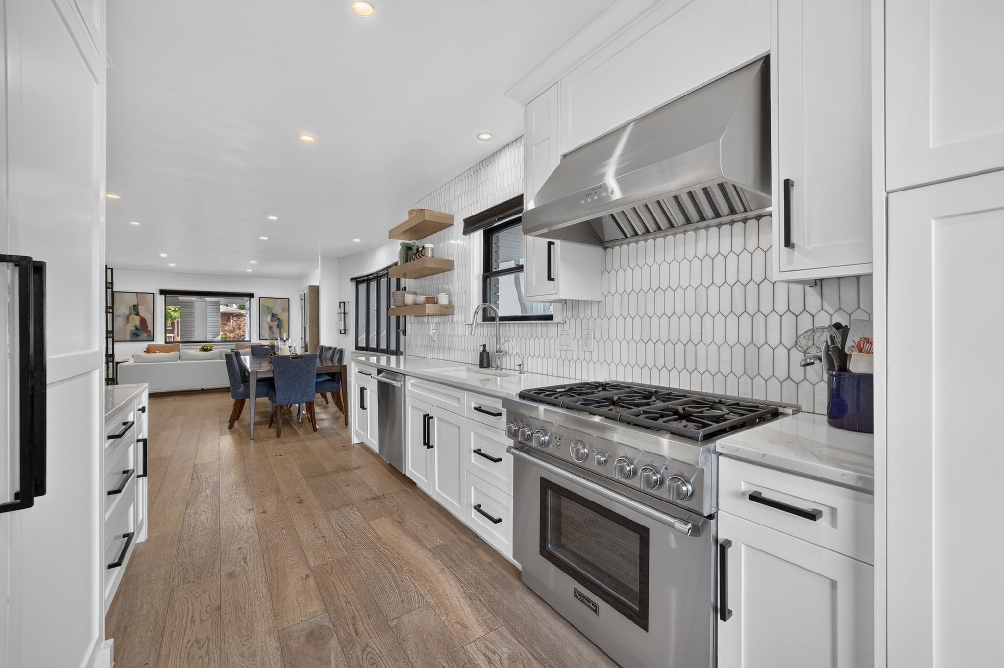 Gourmet kitchen featuring a stainless steel range with a professional-grade hood, white shaker cabinetry, wood-finish flooring, and a patterned tile backsplash