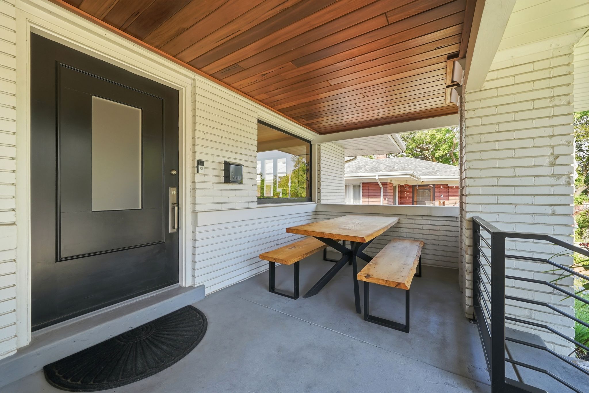 Inviting covered front porch featuring a dark entry door with a frosted glass panel, white horizontal siding, a wood-paneled ceiling, and a concrete floor