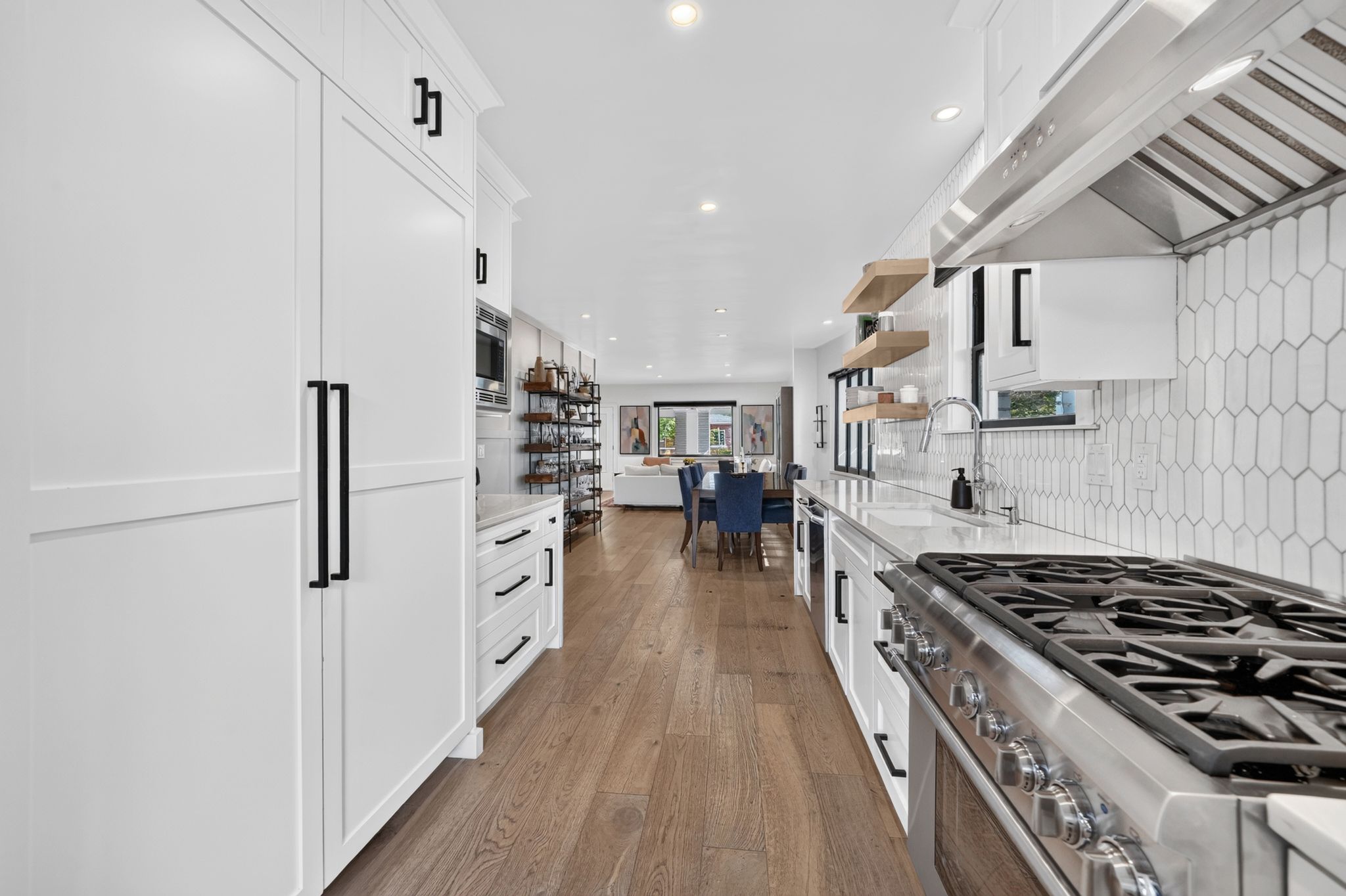 Modern kitchen featuring white cabinetry with black hardware, stainless steel appliances, light wood-finish flooring, and open shelving