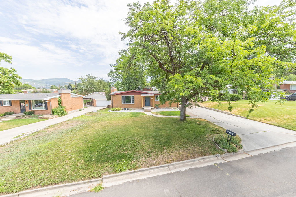 Brick exterior home featuring a mature shade tree, a driveway, and a front lawn