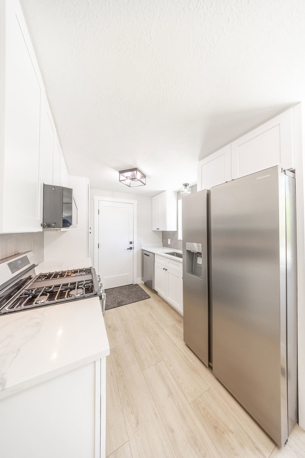 Modern kitchen featuring stainless steel appliances, light wood-finish flooring, white cabinetry, and white countertops