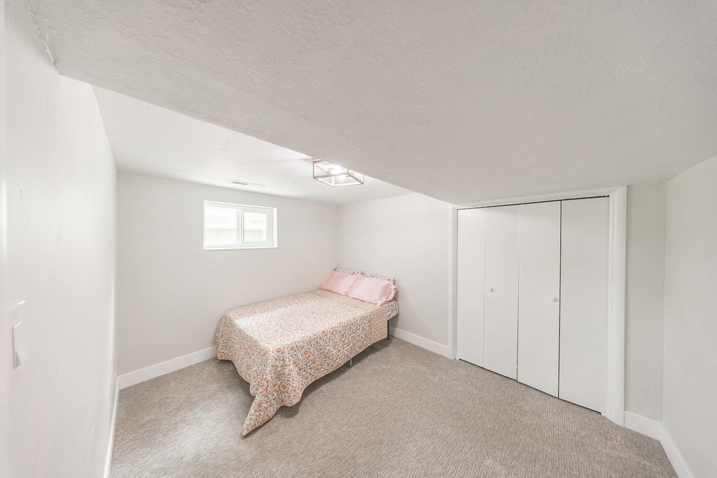 Carpeted room featuring a white window, bi-fold closet doors, white baseboards, and a ceiling-mounted light fixture