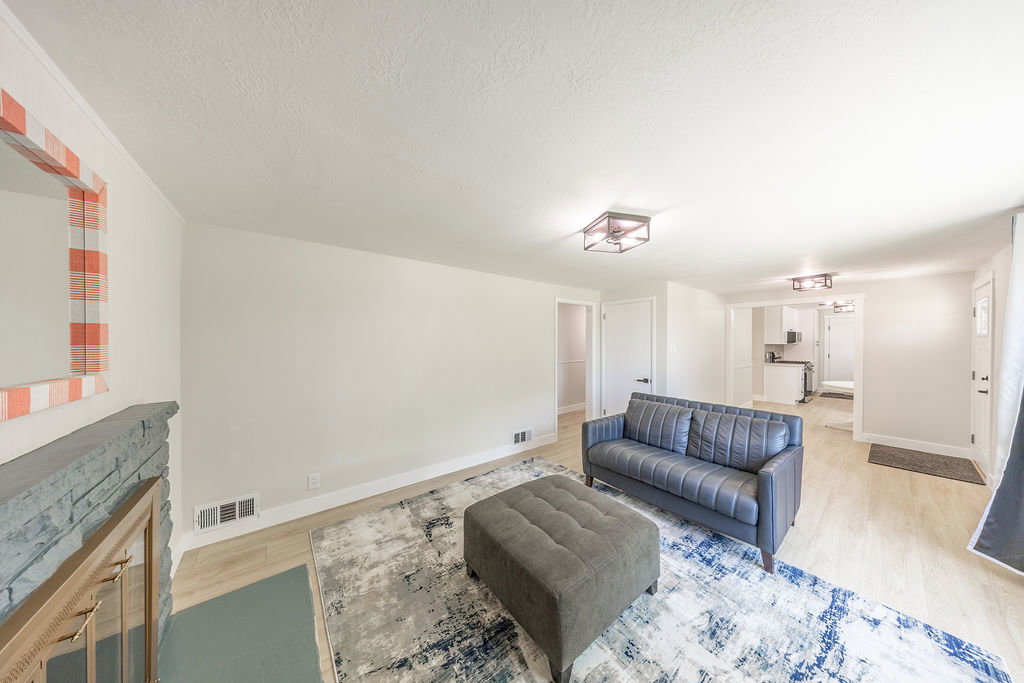 Living area featuring light-tone wood-finish flooring, a painted brick fireplace, and contemporary flush-mount lighting fixtures