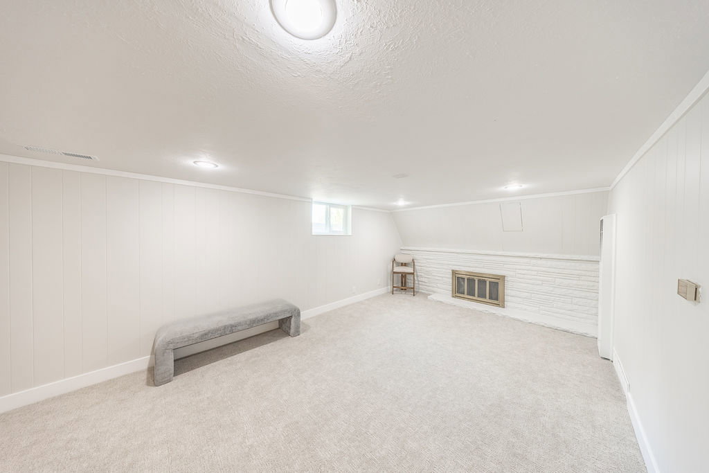 Spacious room with plush carpeting, recessed lighting, white vertical paneling, and a painted brick fireplace with a metal insert