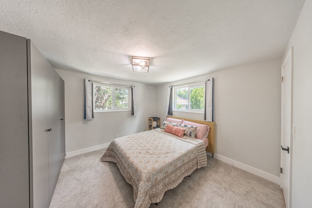 Carpeted room featuring built-in gray wardrobes with black hardware, two windows, and a flush mount ceiling light fixture
