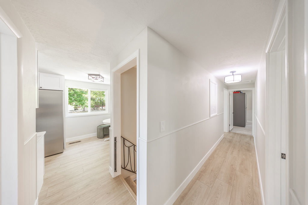 Bright interior hallway with wood-finish flooring, white paneled walls, and recessed lighting