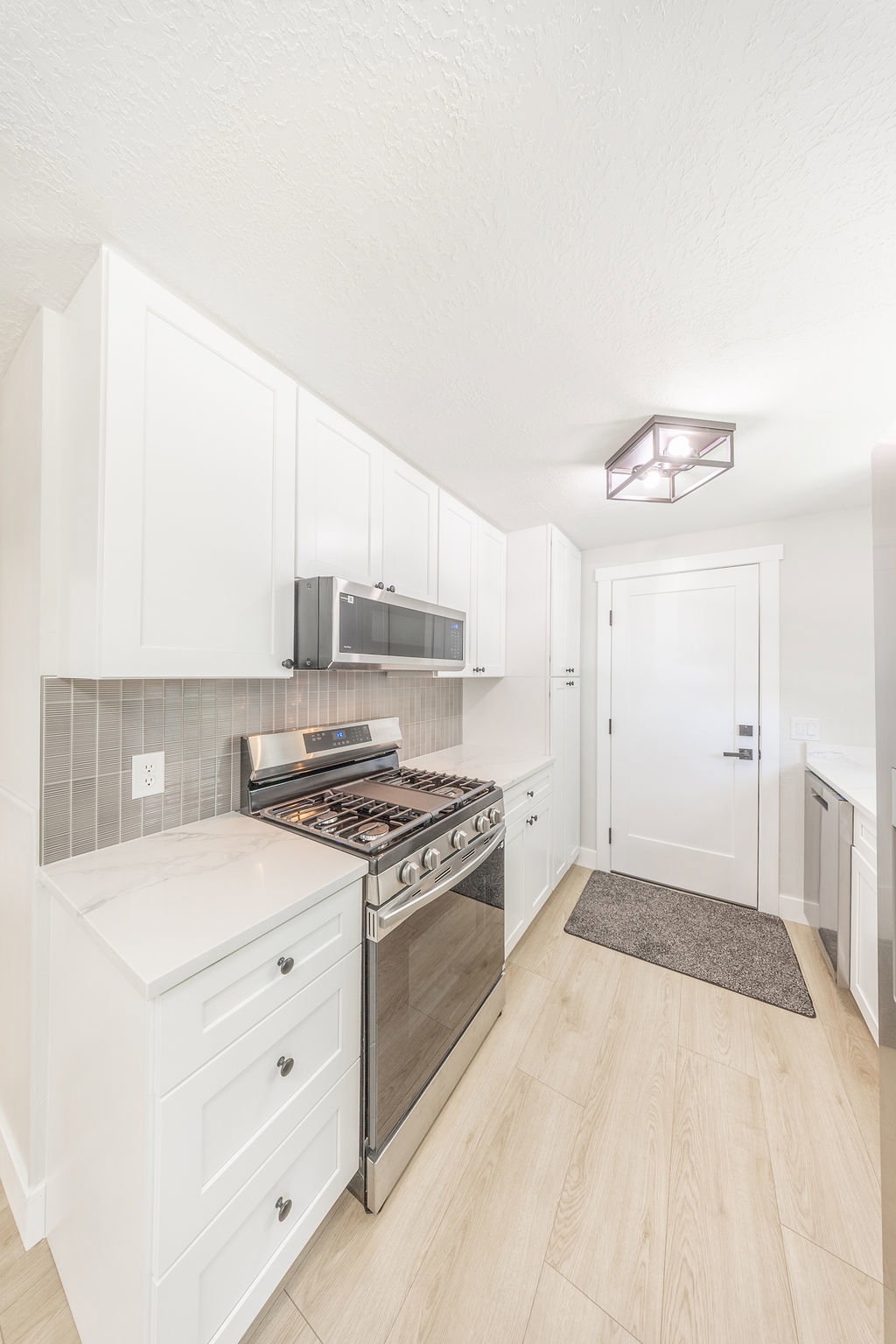 Kitchen featuring white cabinetry, stainless steel range with overhead microwave, light-toned wood-finish flooring, and white countertops