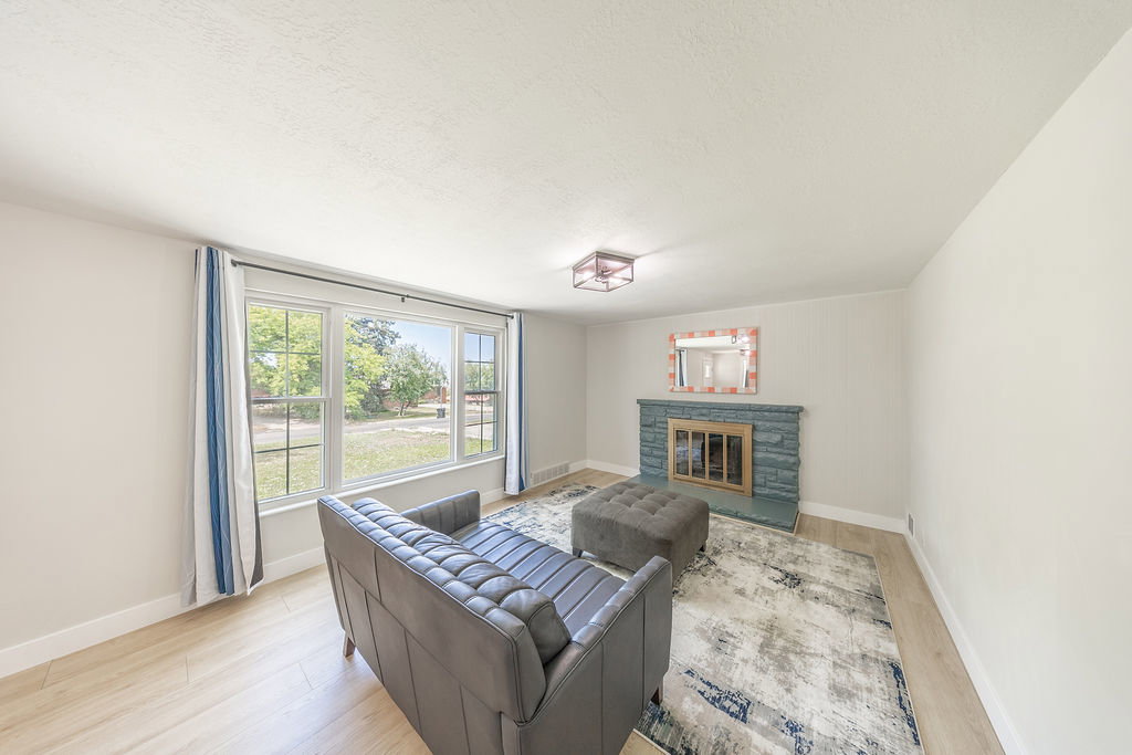 Living space featuring a stone-clad fireplace with hearth, expansive window with grid panes, wood-finish flooring, and a contemporary flush-mount ceiling light fixture