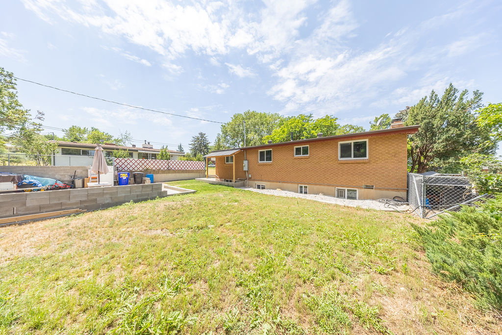Expansive rear yard featuring a brick-clad exterior, multiple windows, a concrete block retaining wall, and a separate storage shed