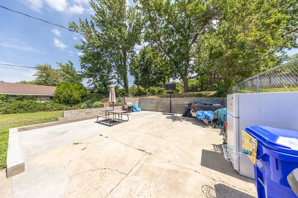Expansive concrete patio area with a block retaining wall and mature trees