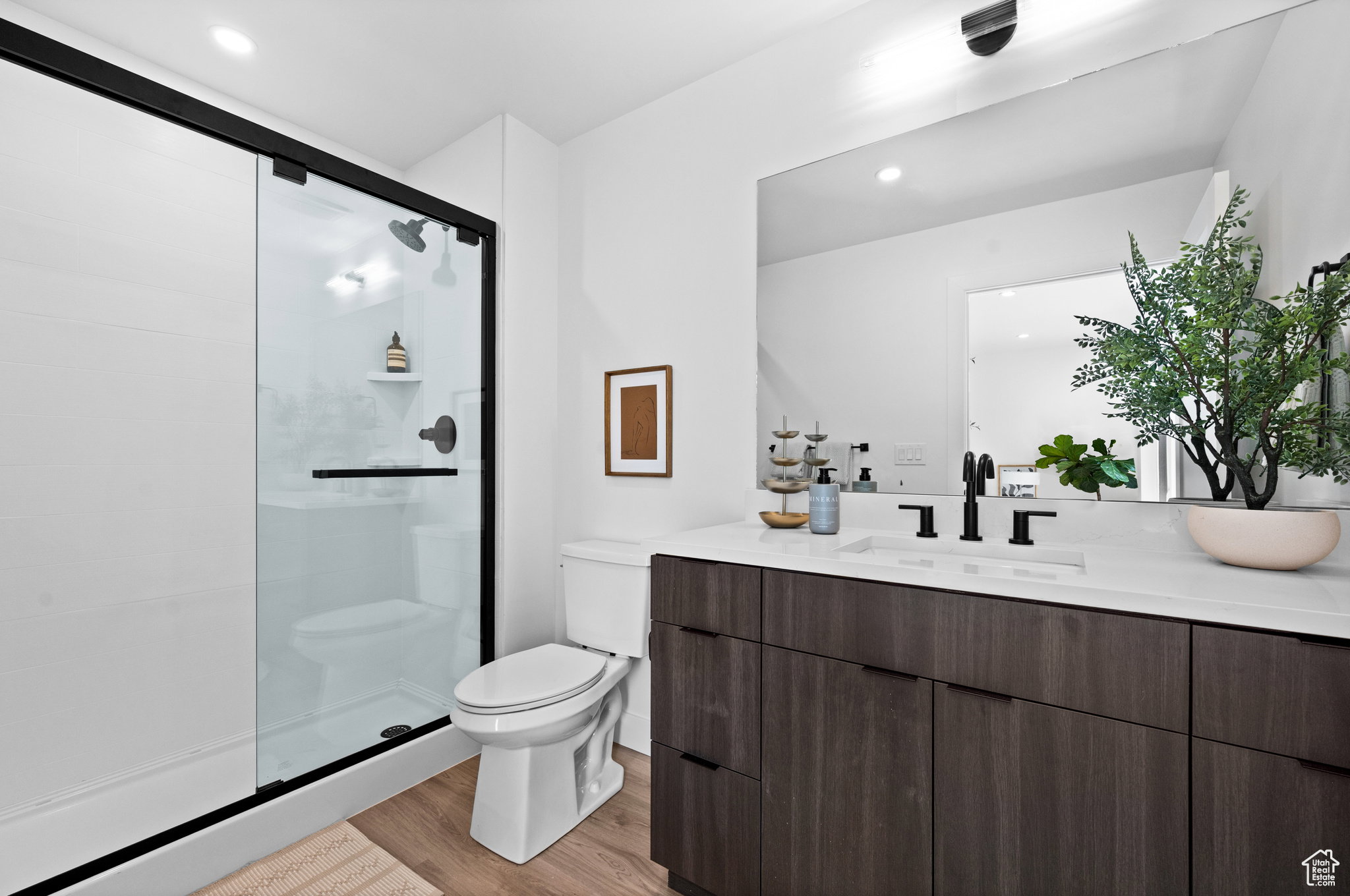 Bathroom featuring a dark wood-finish vanity with an integrated sink and matte black fixtures, a full-width mirror, and a glass-enclosed shower with a black frame and matte black showerhead