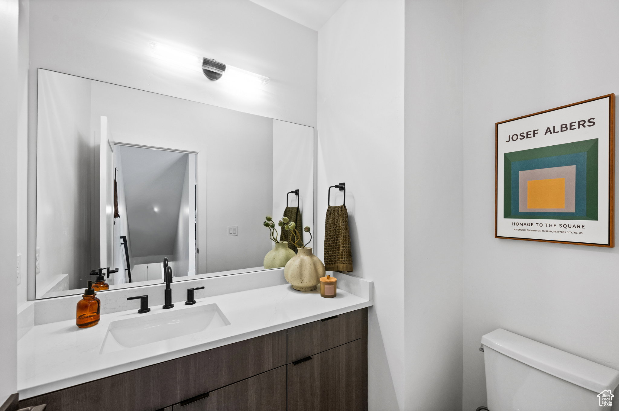 Contemporary vanity featuring a white countertop with an integrated sink and matte black hardware