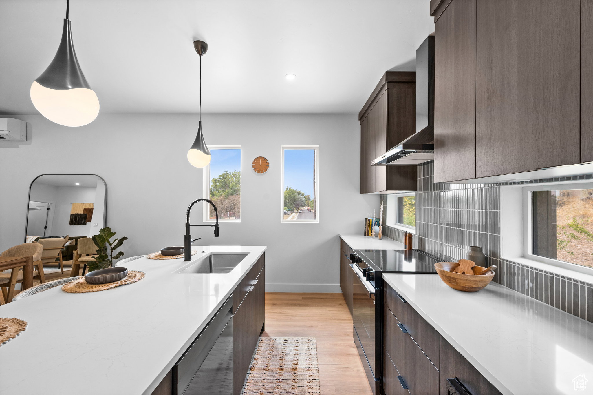 Modern kitchen featuring an island with a built-in sink and matte black faucet, dark wood-finish cabinetry, light countertops, and a tiled backsplash
