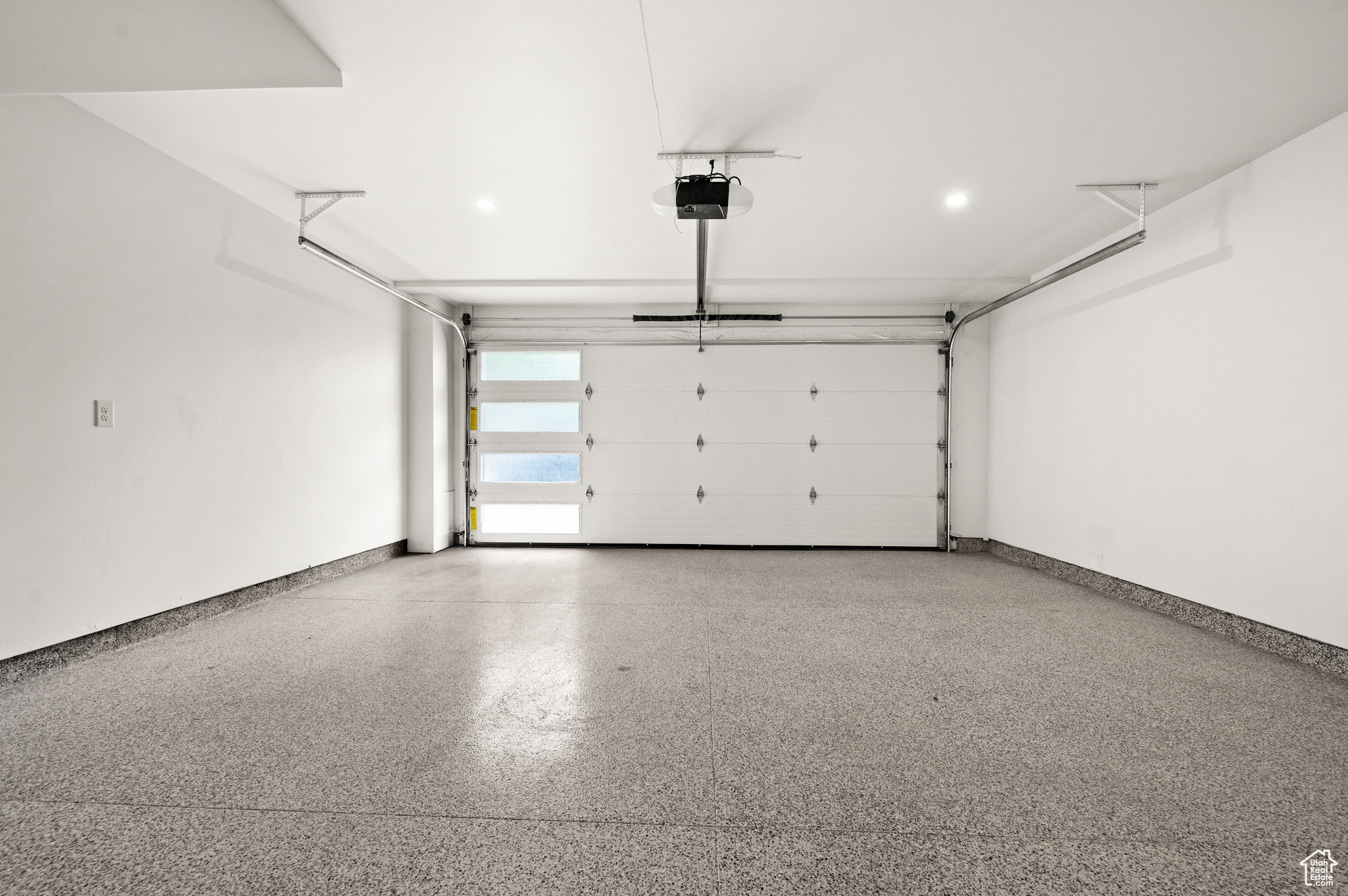 Spacious garage featuring a modern overhead door with frosted glass panels, an epoxy-coated concrete floor, and recessed ceiling lighting
