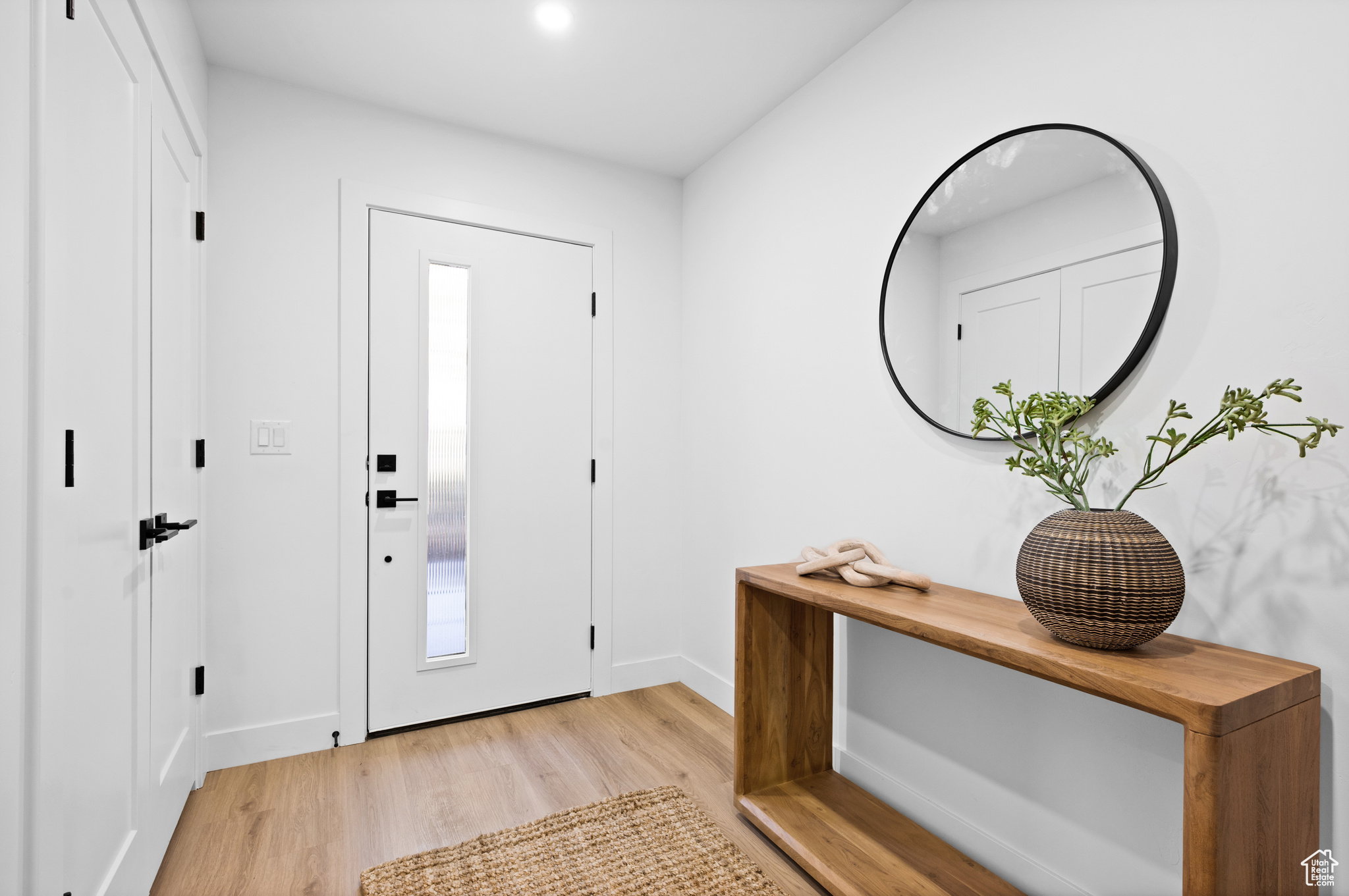 Bright entryway featuring a modern white door with a vertical glass panel, matte black hardware, and light wood-finish flooring