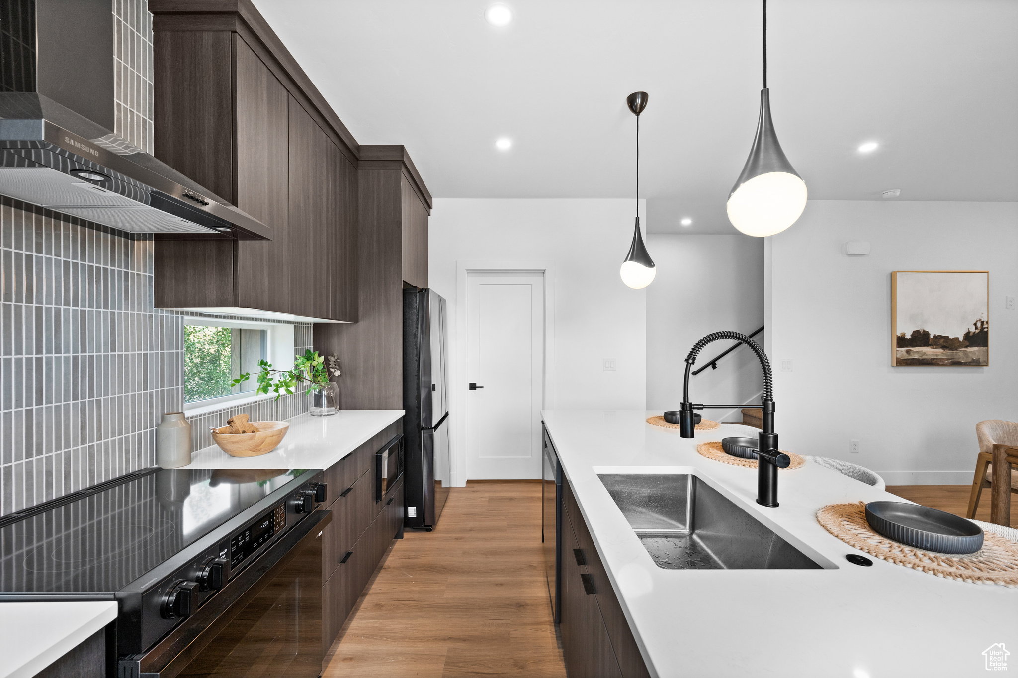 Modern kitchen featuring dark wood-finish cabinetry, light stone countertops, integrated stainless steel appliances, and wood-finish flooring