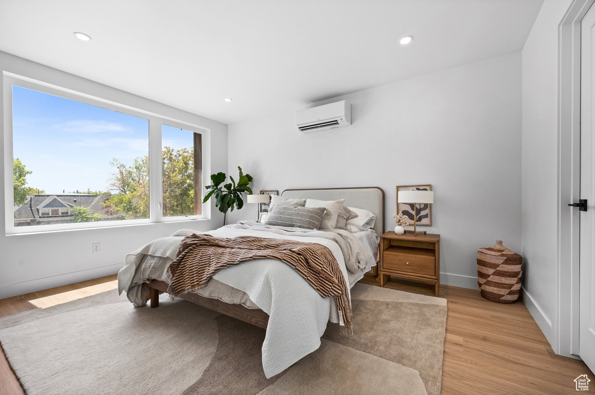 Expansive windows providing natural light, recessed lighting, wood-finish flooring, white walls, and a wall-mounted air conditioning unit