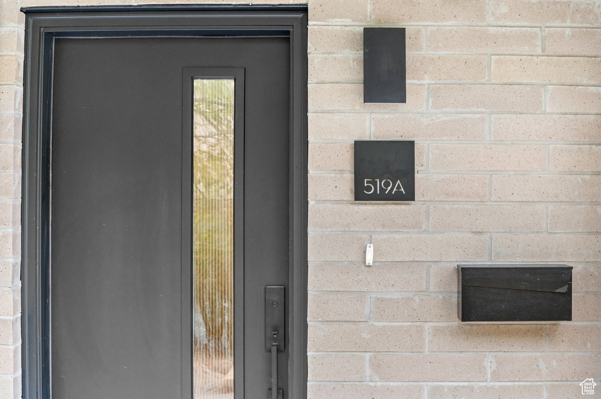 Modern dark entry door with a vertical reeded glass insert, complemented by a light brick facade