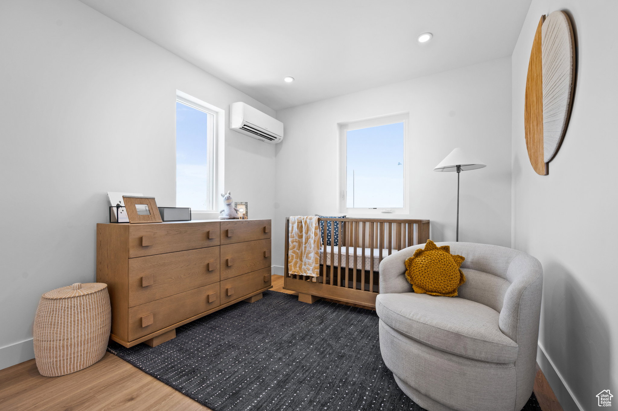 Bright room featuring two windows, recessed lighting, wood-finish flooring, a wall-mounted climate control unit, and white baseboards