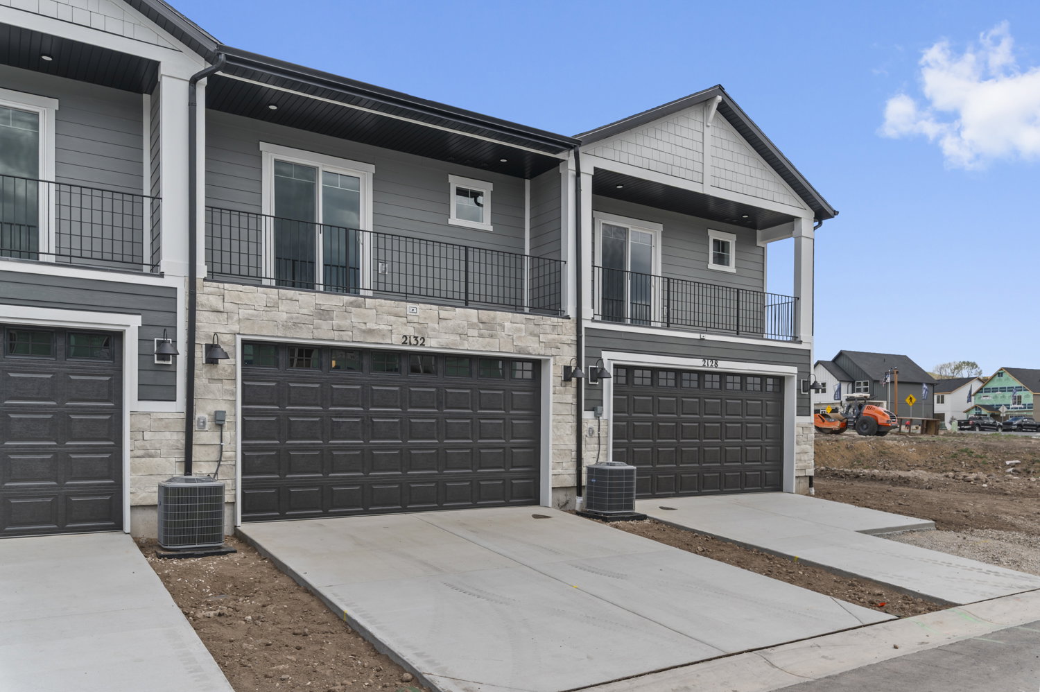 Modern townhome exterior featuring gray siding, stone accents, black garage doors, and upper-level balconies with wrought iron railings
