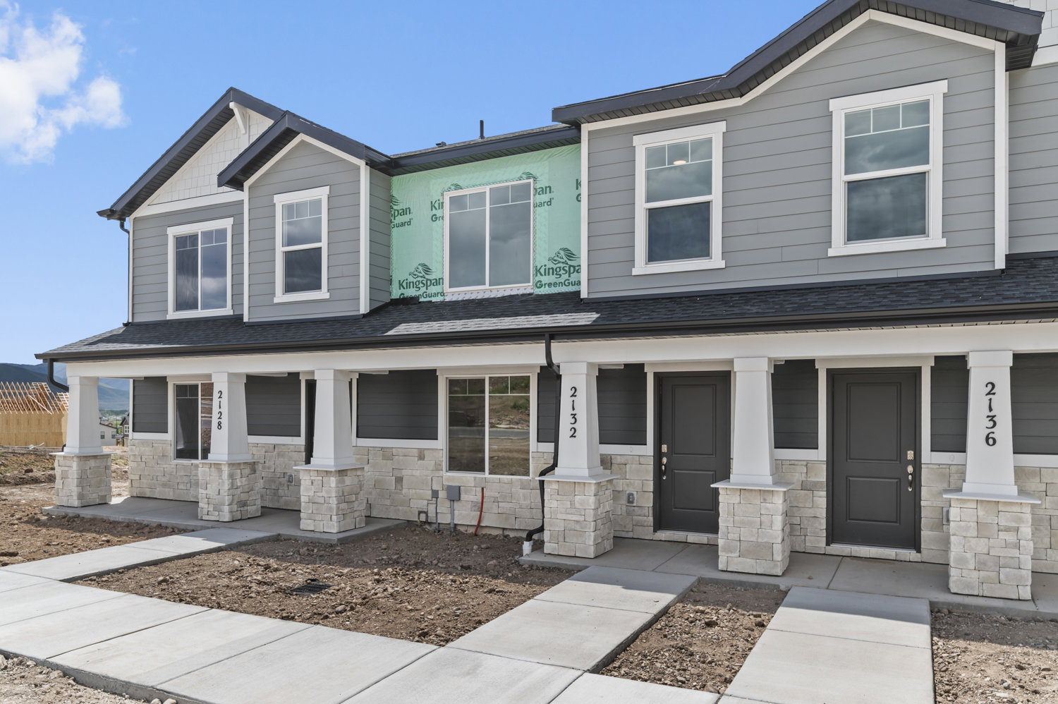 Modern townhome exterior featuring gray siding, white trim, and stone accents