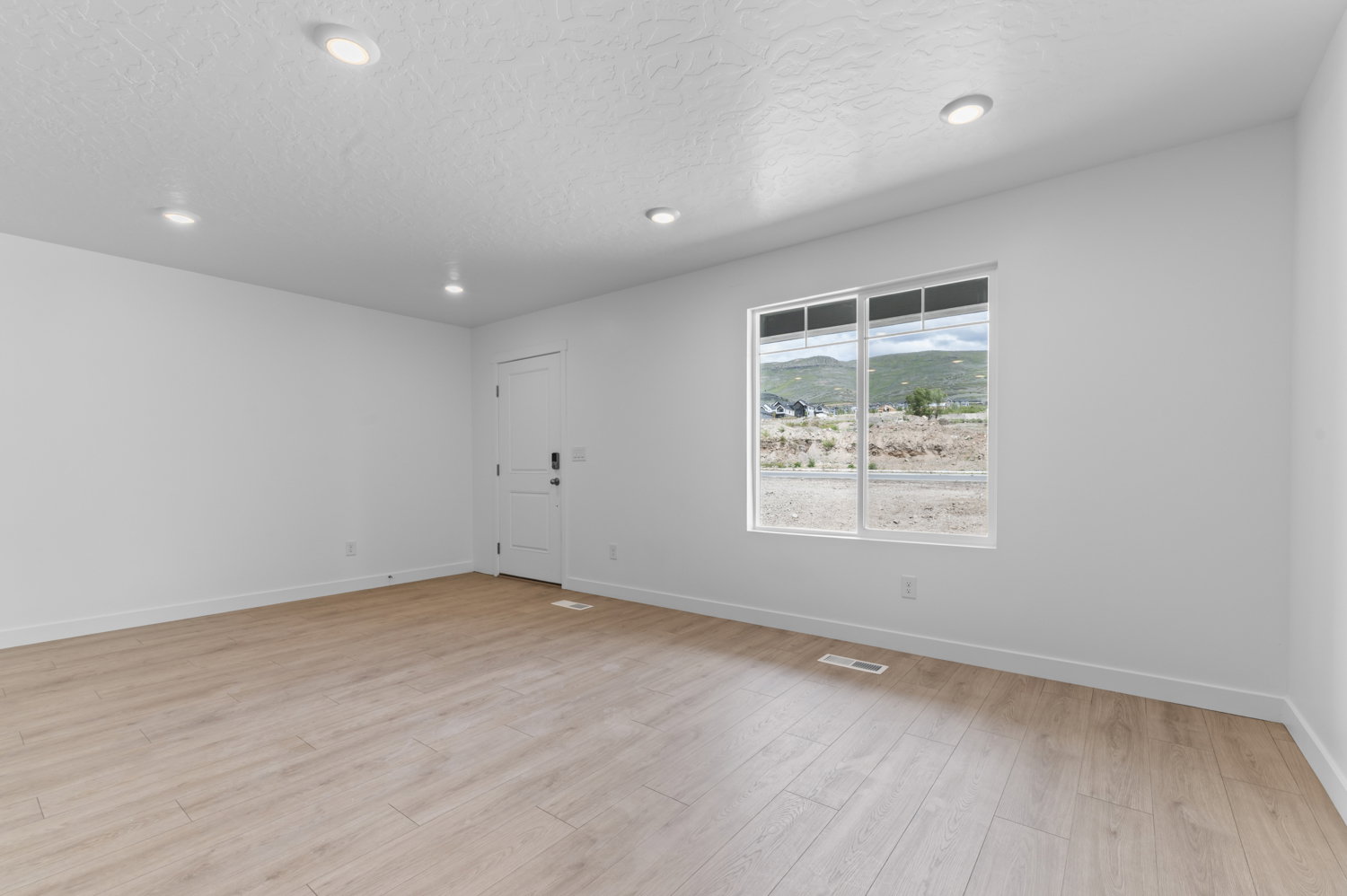Spacious room featuring light wood-finish flooring, recessed lighting, white baseboards, and a large window providing natural scenery