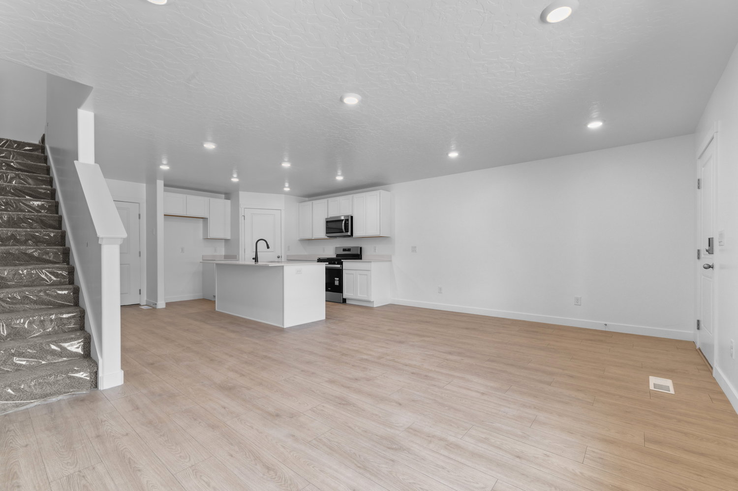 Open-concept living space featuring wood-finish flooring, recessed lighting, and a kitchen with white cabinetry, a central island, and stainless steel appliances