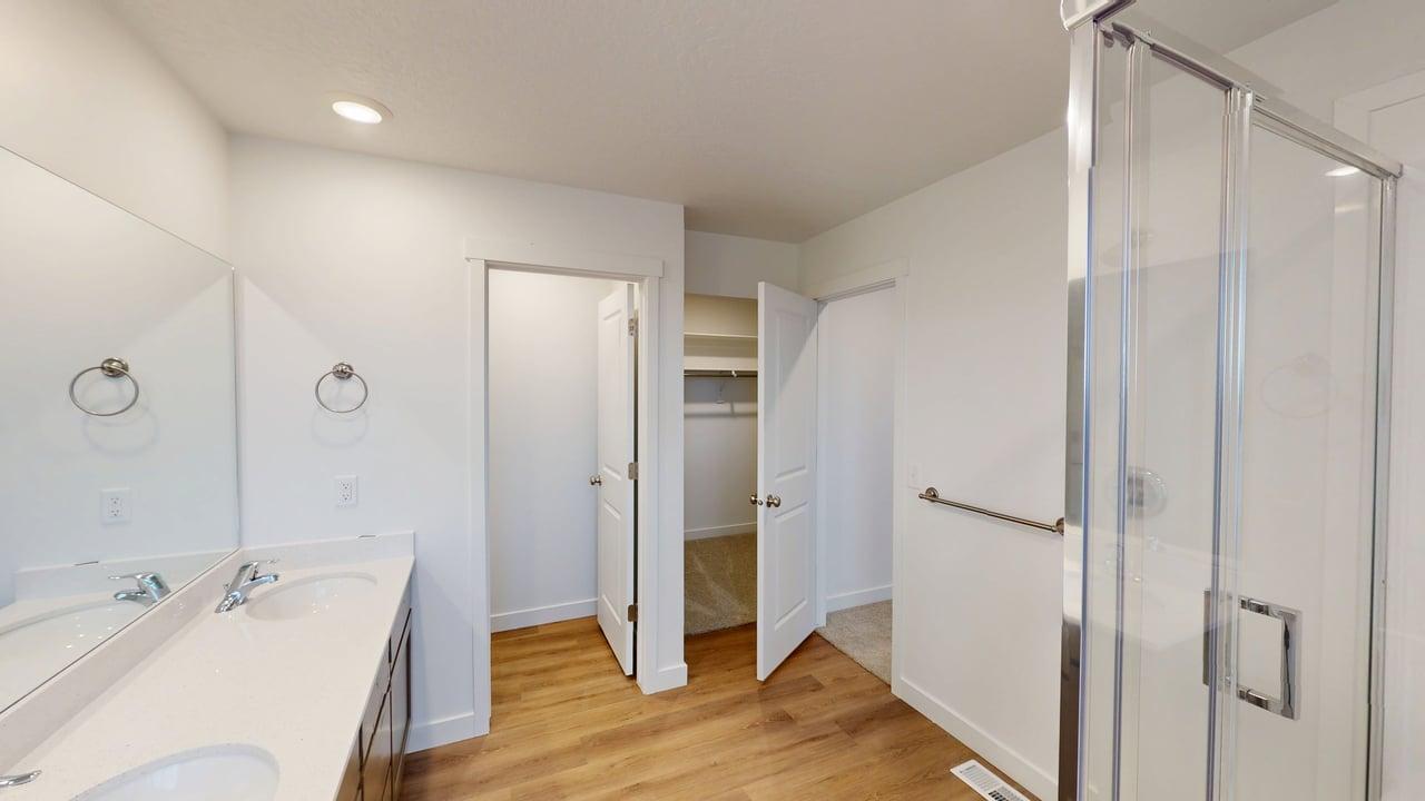 Bathroom featuring a double vanity with integrated sinks, a glass-enclosed shower, wood-finish flooring, and recessed lighting