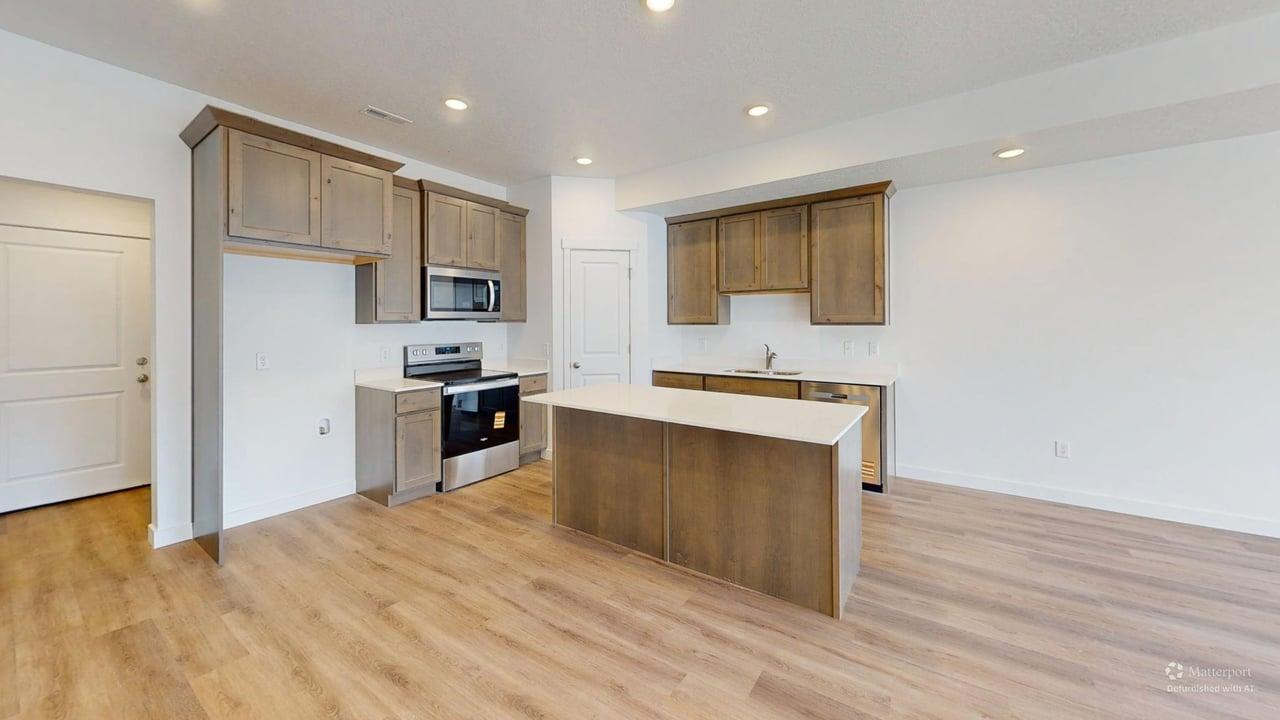 Modern kitchen featuring wood-finish flooring, recessed lighting, a central island with a light-toned countertop, and stainless steel appliances including a range, microwave, and dishwasher