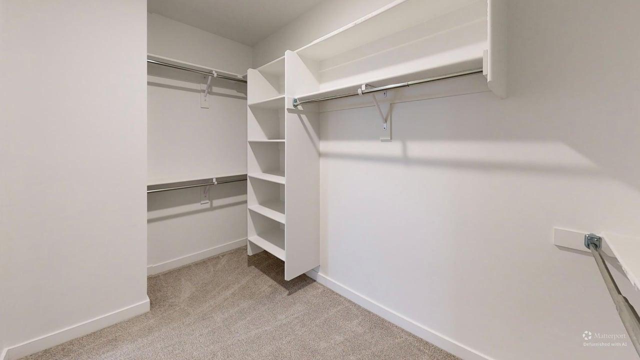 Walk-in closet featuring built-in shelving, multiple hanging rods, light-toned carpeting, and crisp white walls
