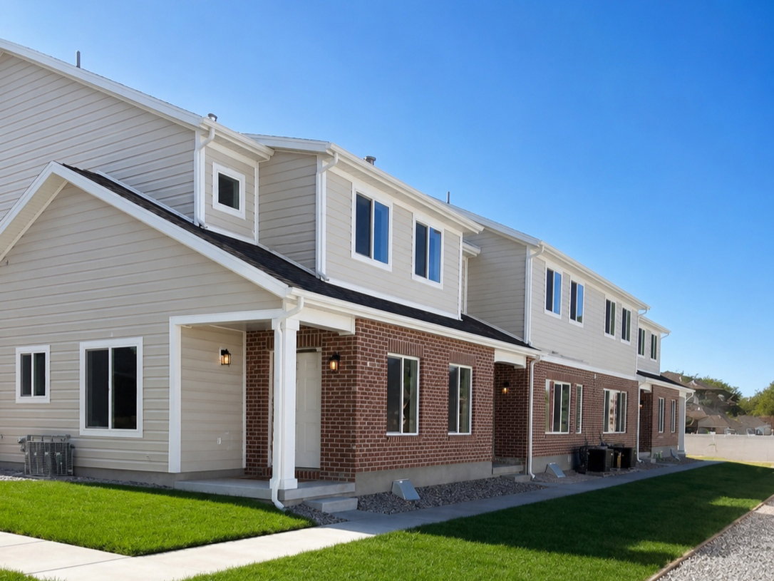 Contemporary townhome exterior featuring brick and siding facade, covered entryways, multiple windows, and a manicured lawn
