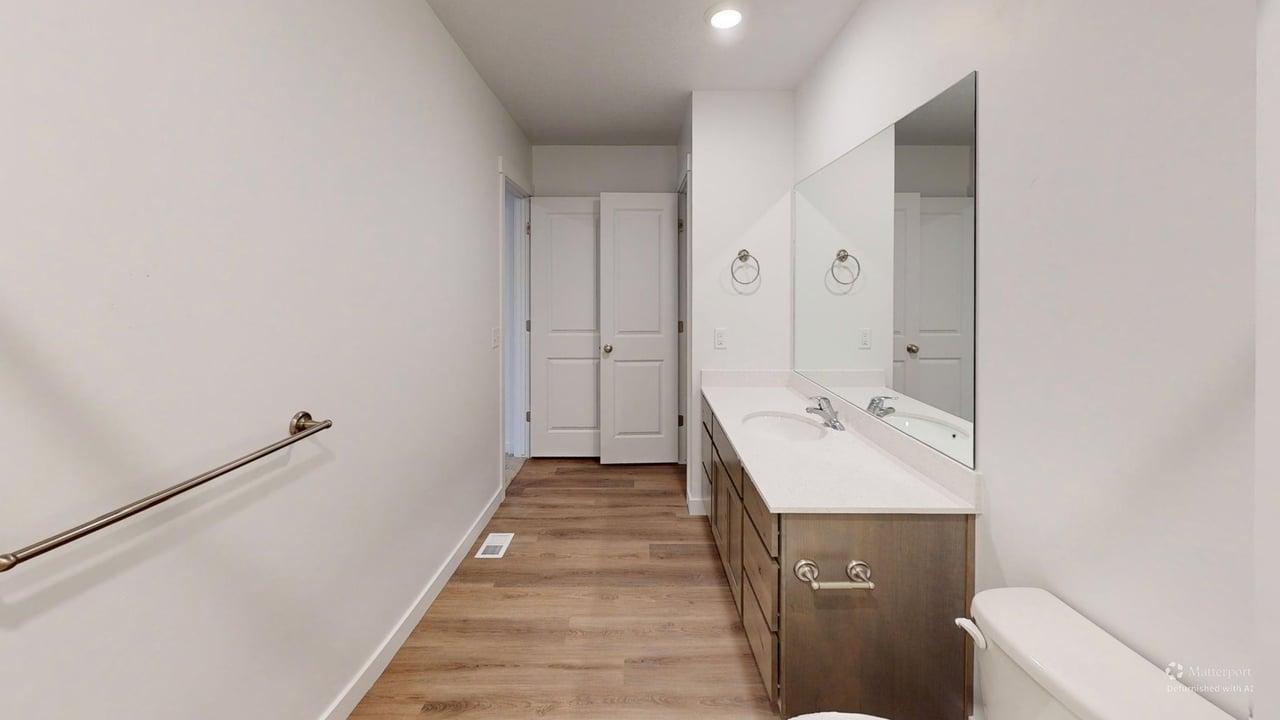 Bathroom featuring a double vanity with undermount sinks, a large mirror, a toilet, and wood-finish flooring