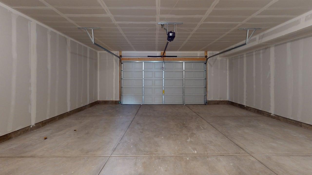 Spacious garage featuring a concrete floor, an overhead garage door opener, and unfinished drywall walls