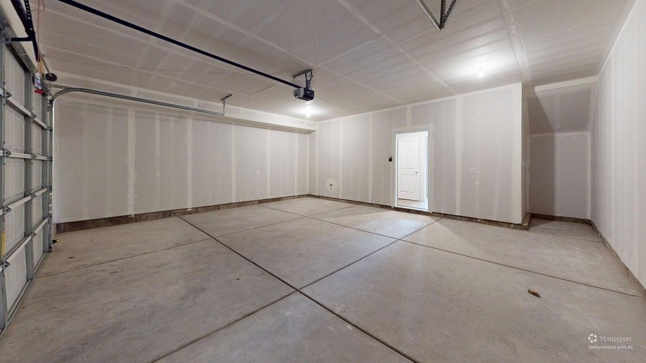 Spacious garage with exposed drywall, concrete flooring, and an overhead garage door