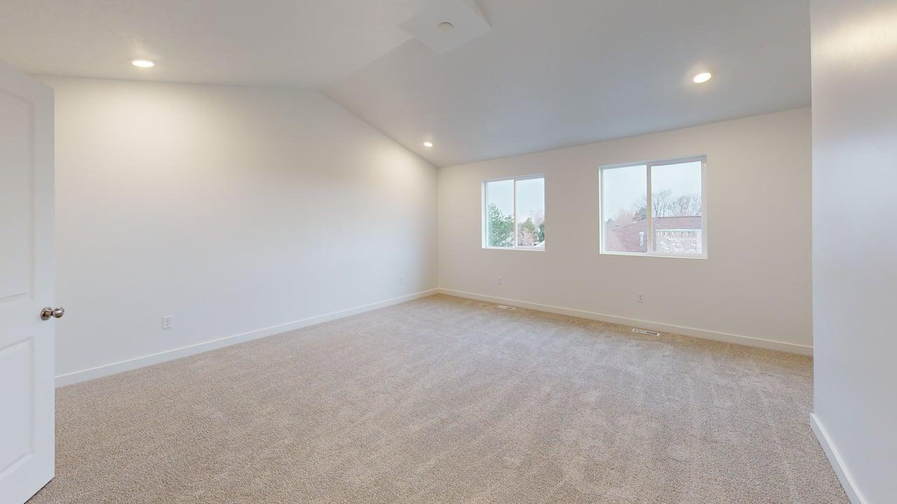 Spacious room featuring vaulted ceilings, recessed lighting, two windows with white trim, and light-colored carpet flooring