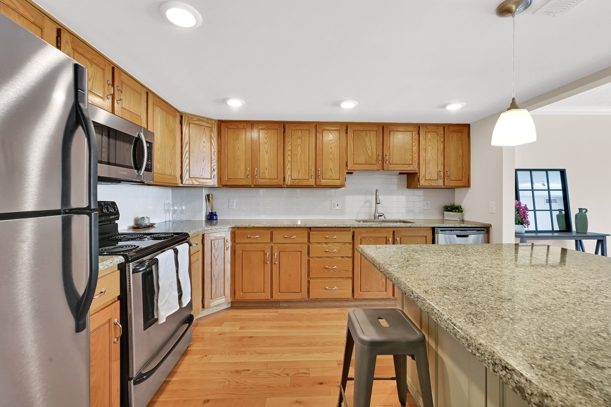Kitchen featuring light wood cabinetry, granite countertops, stainless steel appliances, a subway tile backsplash, and wood-finish flooring