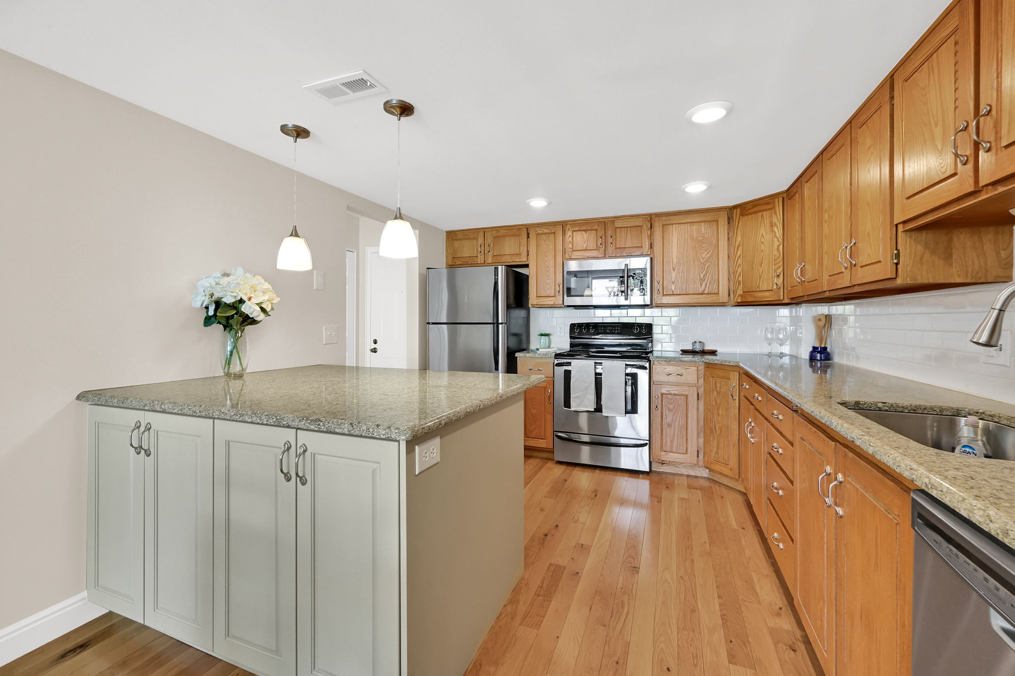 Kitchen featuring wood-finish flooring, light-colored granite countertops, and a white subway tile backsplash