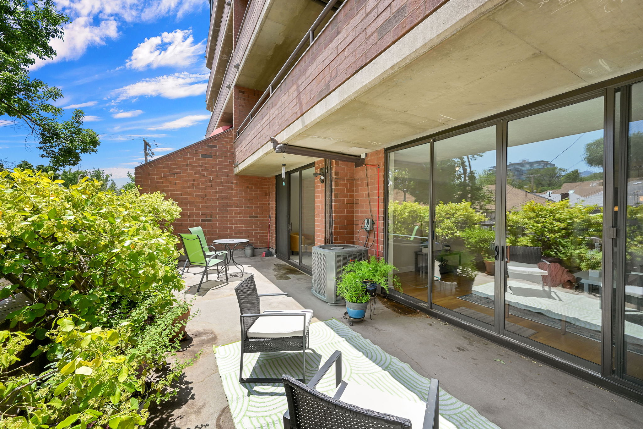 Private concrete patio featuring mature landscaping, brick exterior, and full-height sliding glass doors