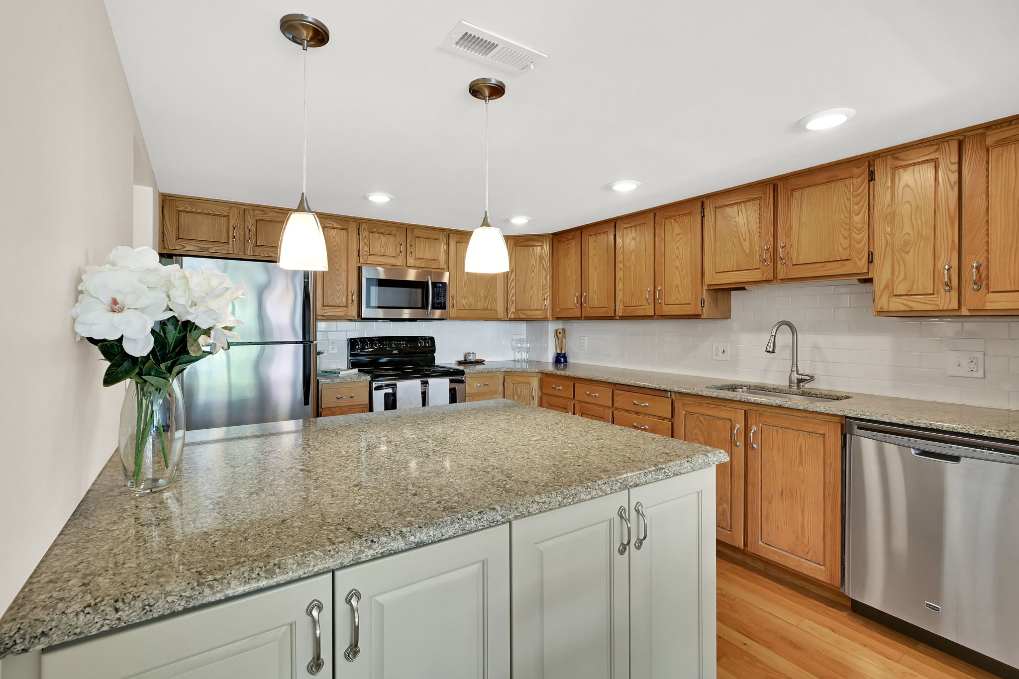 Kitchen featuring an island with granite countertop, wood-finish flooring, stainless steel appliances, and wood cabinetry