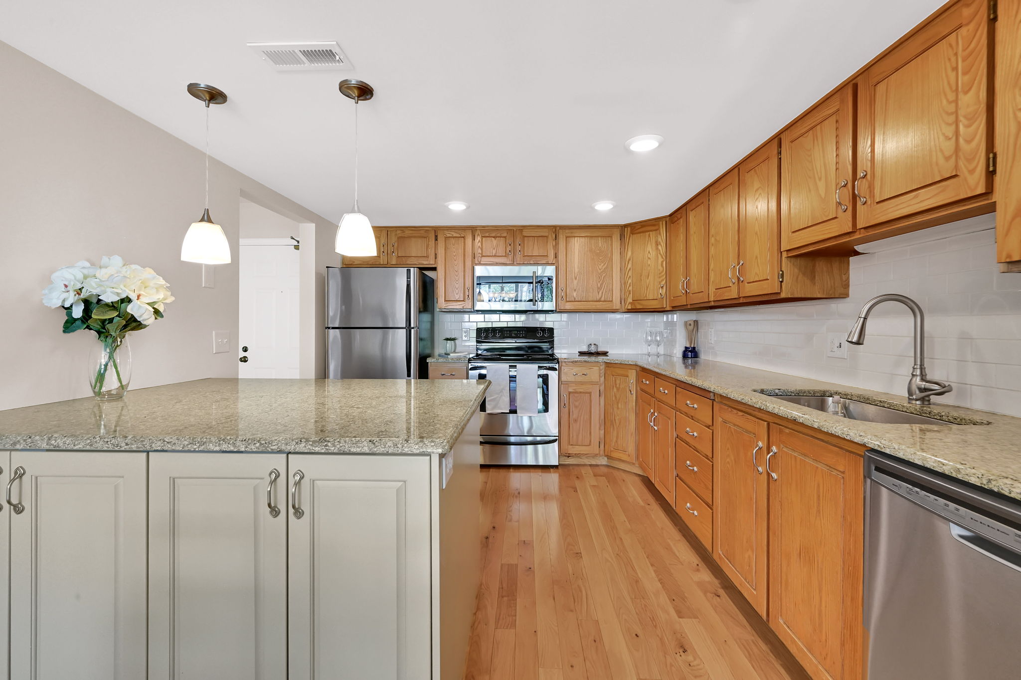 Kitchen featuring wood-finish flooring, stainless steel appliances, light wood cabinetry, and granite countertops