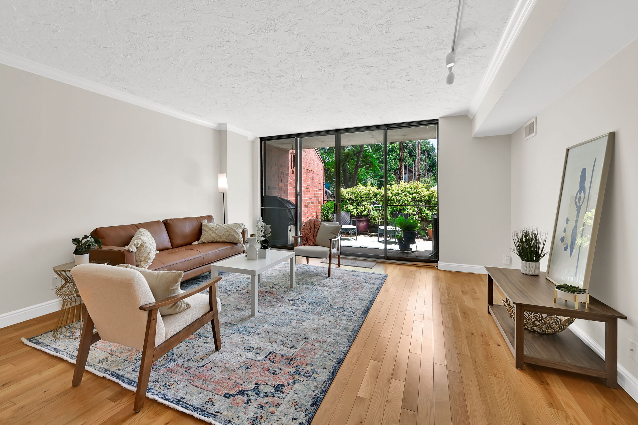 Living area featuring wide plank wood flooring, track lighting, crown molding, and a full wall of sliding glass doors opening to a private patio